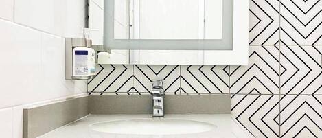 A bathroom with a rectangular sink, a mirror, and a patterned tile backsplash.