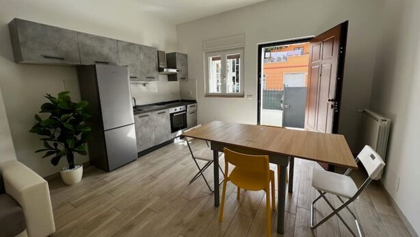 Una cocina moderna con armarios grises, horno empotrado y comedor con mesa de madera y dos sillas.