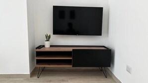 Una sala de estar moderna con un televisor de pantalla plana montado en la pared, un mueble de madera con un cajón, y una pequeña planta en maceta sobre el mueble.