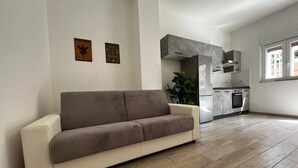 Una sala de estar moderna con un sofá, una cocina equipada y un gran ventanal.