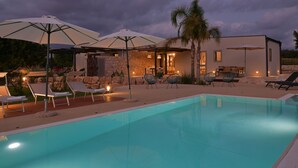 A modern outdoor pool area with lounge chairs, umbrellas, and a stone wall. - VILLA RARIKI, POOL AND RELAX (Scicli)