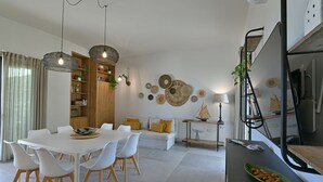 A modern living room with a dining area, featuring a white table, chairs, and a sofa with yellow cushions. There are decorative wall art pieces and a bookshelf with plants. - VILLA RARIKI, POOL AND RELAX (Scicli)