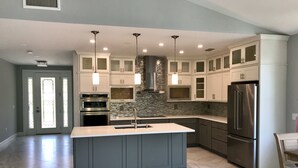 A modern kitchen with a central island, stainless steel appliances, and a stone backsplash. - Private heated pool & spa home. Close to beach! (Naples)
