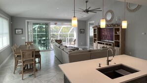 A modern kitchen with a central island, a dining area with a table and chairs, and a living area with a sofa and TV. - Private heated pool & spa home. Close to beach! (Naples)