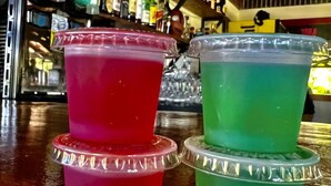 Dois copos de plástico empilhados, com tampas, um vermelho e um verde, em um balcão de bar.