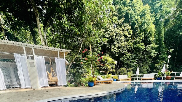 Piscina com água azul cristalina, cercada por uma área de estar coberta com cortinas brancas e plantas em vasos.