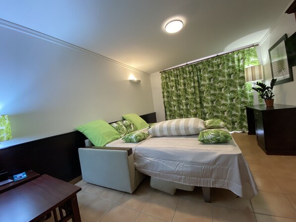 A bedroom with a bed, a desk, and a chair. There is a window with curtains and a plant on the desk. - OCEAN DREAM (Sainte-Anne)