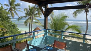 Restaurante à beira-mar com mesas ao ar livre, com vista para o oceano e palmeiras.