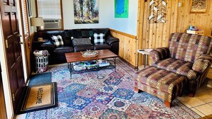 A living room with a black leather sofa, patterned armchair, and a colorful rug. - Charming Fall Cabin on Lake Mille Lacs; Relax, Fish & Watch the Sunset (Isle)