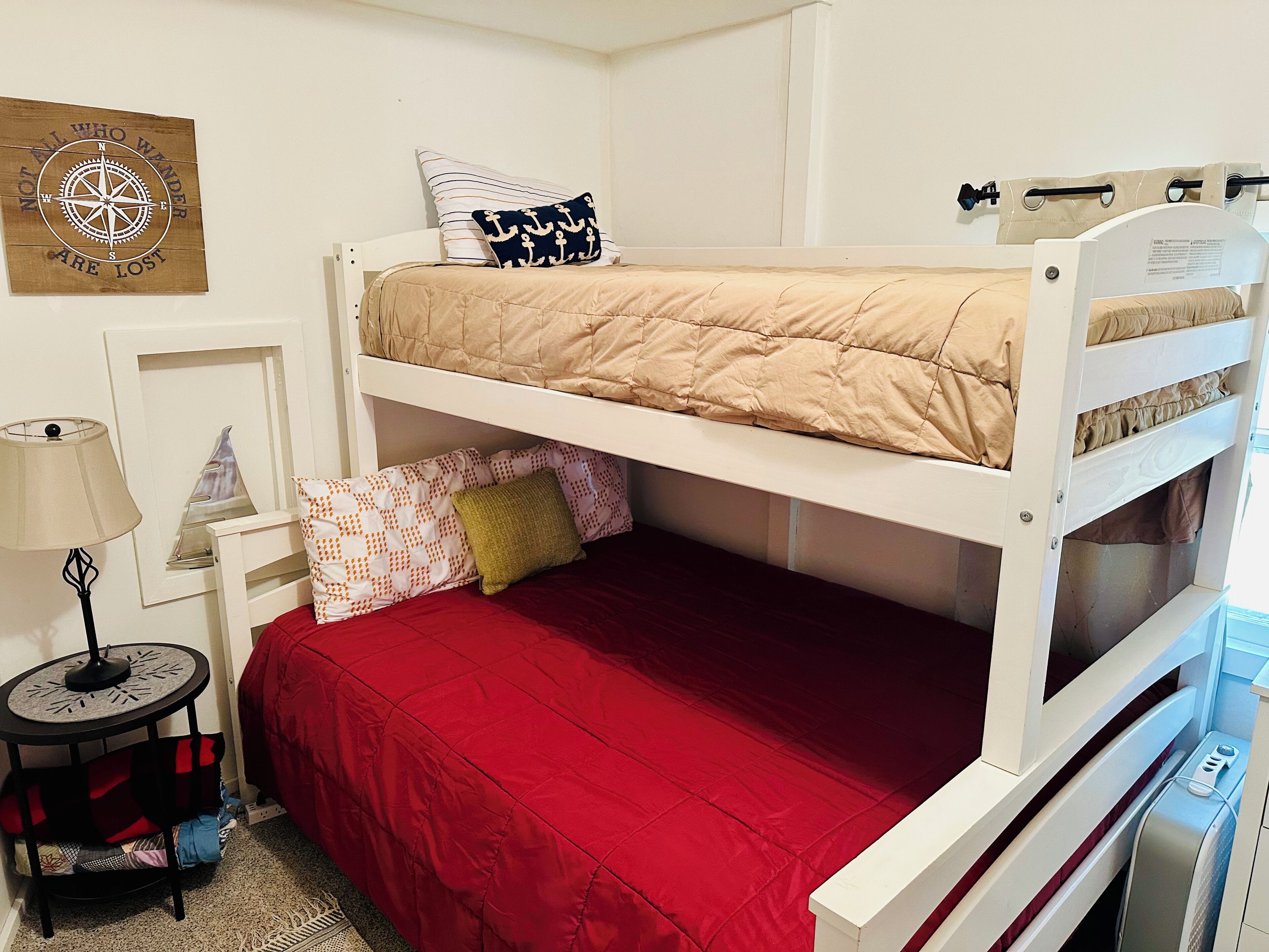 Une chambre avec un lit superposé, une couvre-lit rouge, une décoration murale sur le thème de la boussole, une lampe et une petite table avec un miroir.