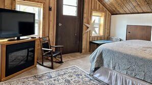 A cozy room with a wooden ceiling, a bed, a desk with a television, and a chair. - Charming Fall Cabin on Lake Mille Lacs; Relax, Fish & Watch the Sunset (Isle)