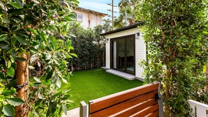 A modern house with a small patio, a wooden bench, and lush greenery.