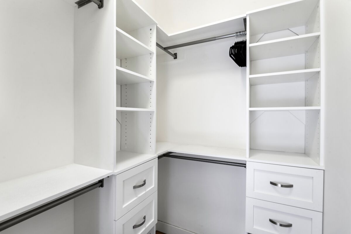 Een witte kast met meerdere planken en lades, voorzien van een metalen hangroede.