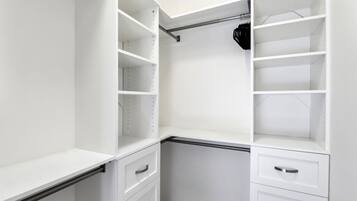 Een witte kast met meerdere planken en lades, voorzien van een metalen hangroede.