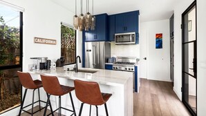 A modern kitchen with blue cabinets, stainless steel appliances, and a white island with bar stools.