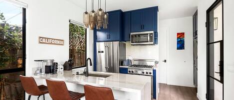 Una cocina moderna con gabinetes azules, electrodomésticos de acero inoxidable y una isla blanca con taburetes.