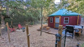 Une yourte avec un toit bleu, entourée d’une terrasse en bois, de tables de pique-nique et de chaises rouges.