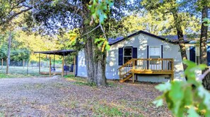 A cabin with a wooden deck, surrounded by trees and a gravel path.