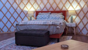 Un dormitorio con cama, mesitas de noche, un banco y una alfombra.
