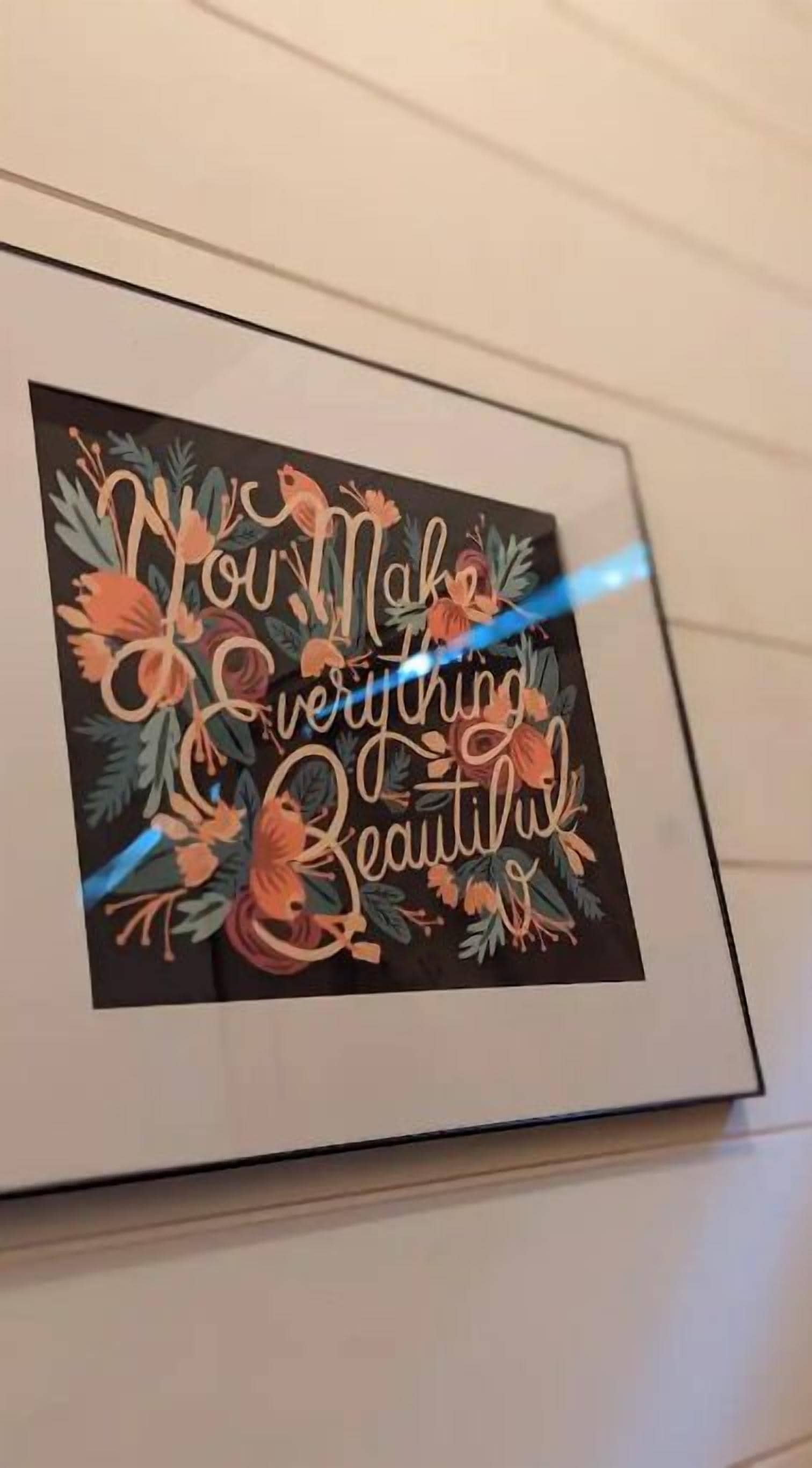 Une œuvre d’art encadrée, portant l’inscription « Vous embellissez tout », le tout agrémenté de motifs floraux.