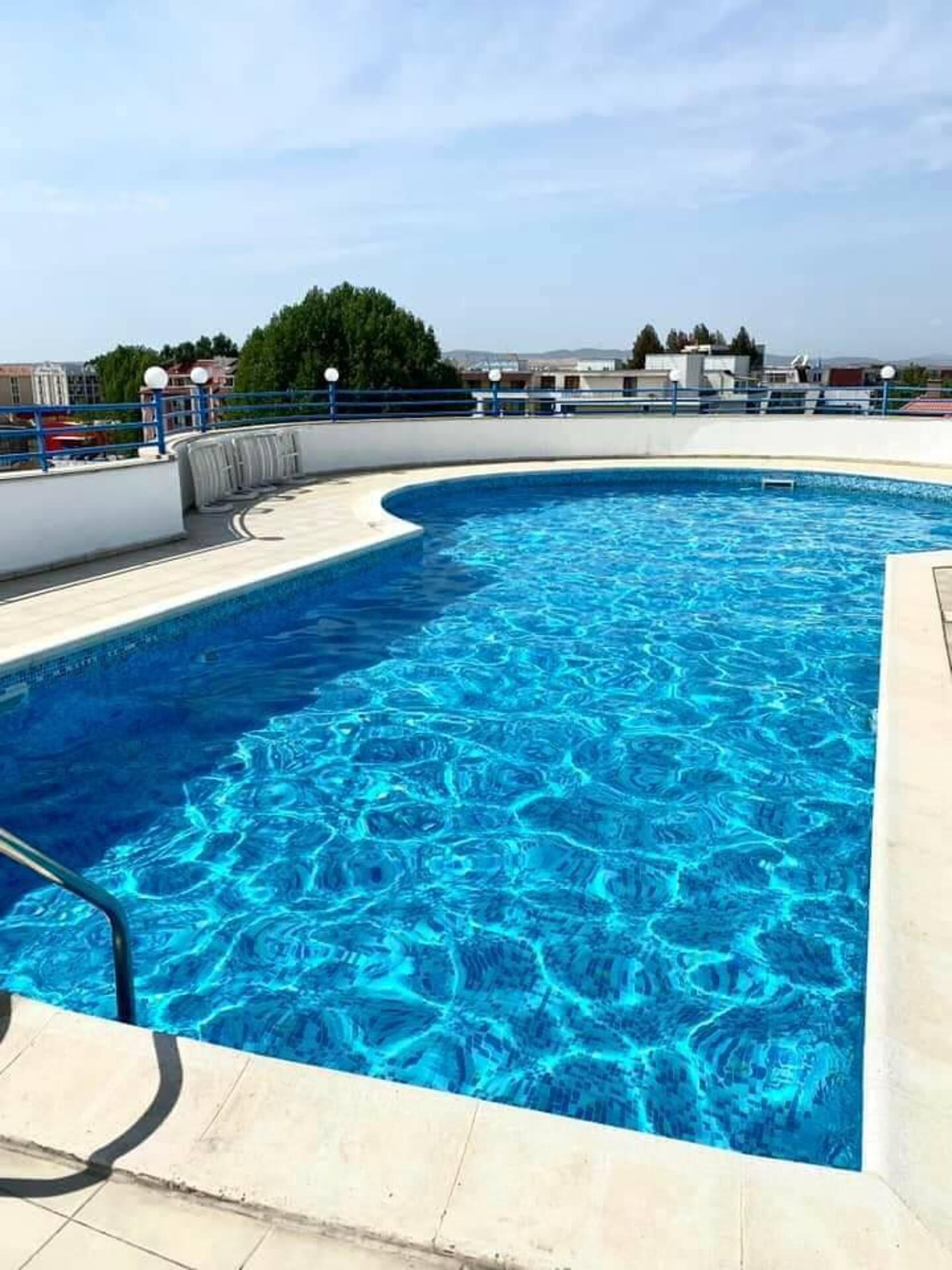 A swimming pool with a curved edge, a diving board, and a clear blue sky in the background.