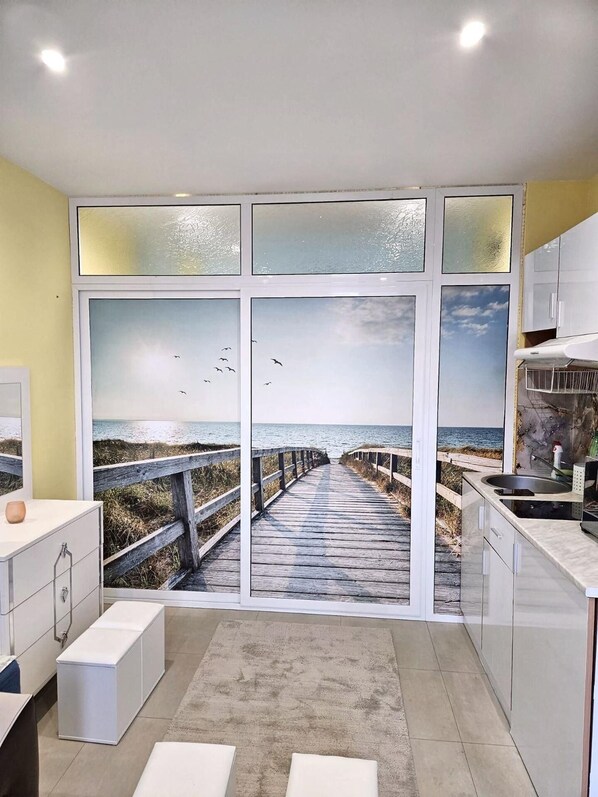 A modern kitchen with a large window overlooking a beach scene.