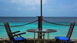 A table with two chairs and an umbrella overlooking a turquoise sea.