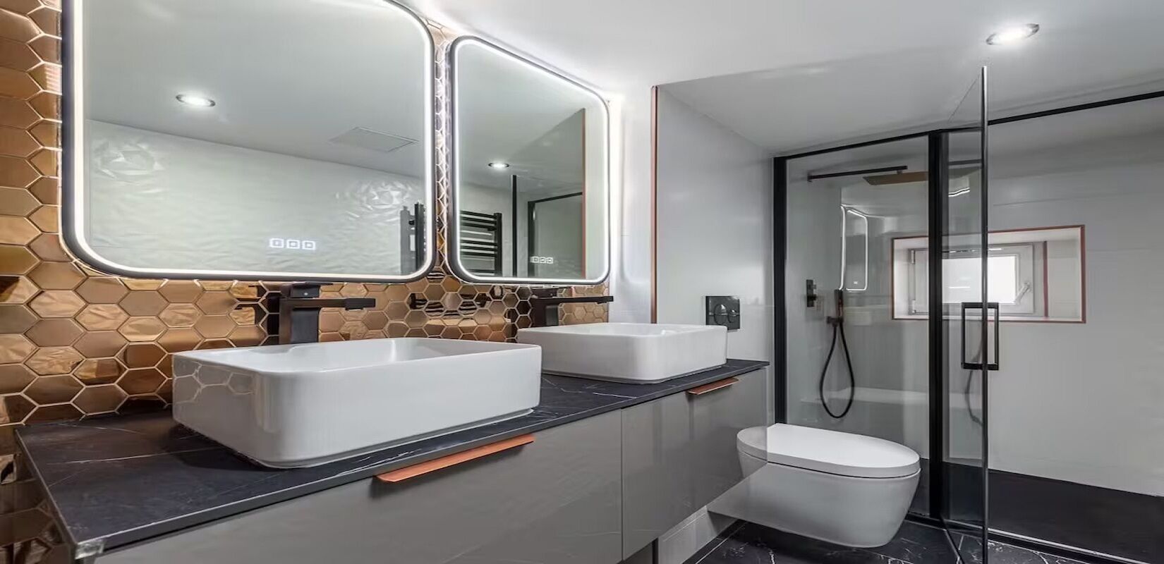 A modern bathroom with two sinks, a toilet, and a glass shower enclosure.