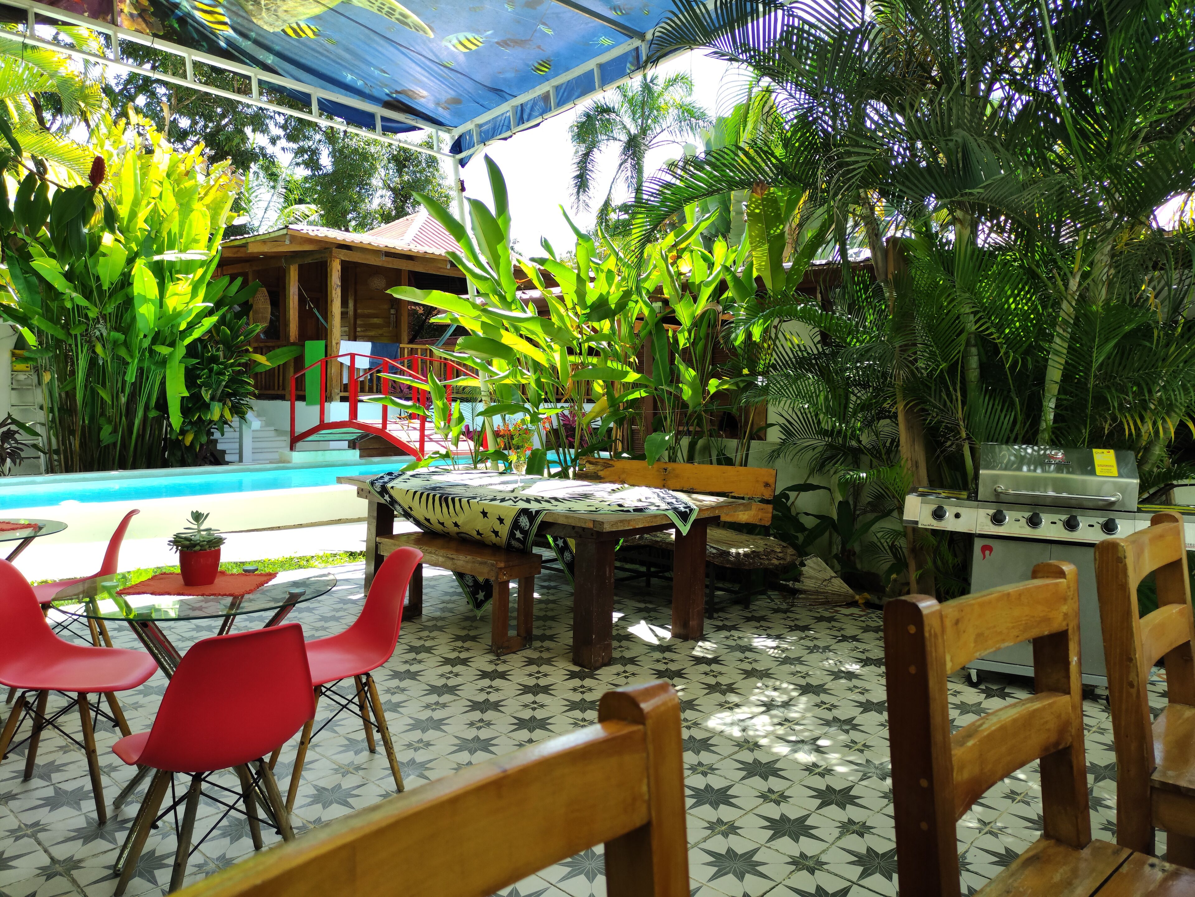 An outdoor patio with a pool, wooden furniture, and a grill area.