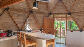 A kitchen with a central island, wooden chairs, a hanging light fixture, and a view of the outside. - Seacret Villa (Cóbano)