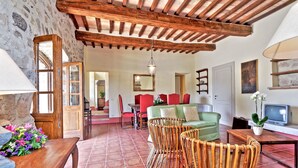 Un intérieur rustique avec un plafond en bois, un sol carrelé, des chaises en osier, un canapé vert et un téléviseur.