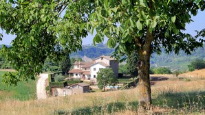 Une maison de campagne, accessible par un chemin de terre, entourée de champs et d’arbres.