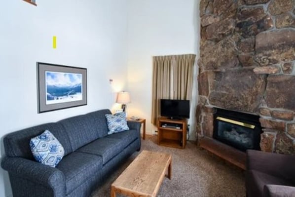 Una sala de estar con chimenea de piedra, un sofá, una mesa de centro y un televisor.