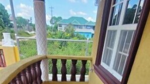 Un balcón con barandillas de madera y suelo de baldosas, con vistas a un paisaje verde.