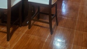 Un coin repas avec une table et des chaises en verre, une cuisine en arrière-plan et un plancher en bois.