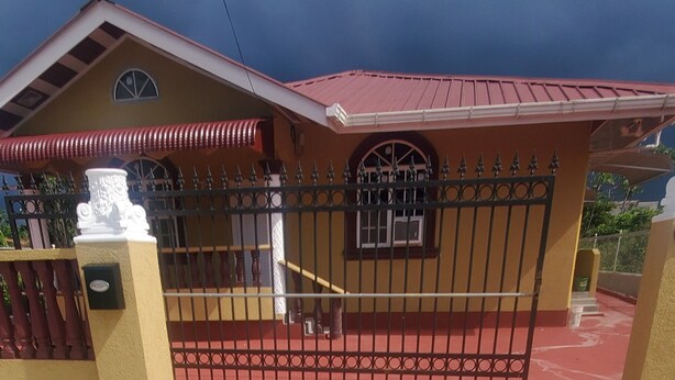 Un bâtiment doté d’une entrée fermée par un portail, d’un toit rouge et d’un chemin pavé aux motifs colorés menant à la porte.