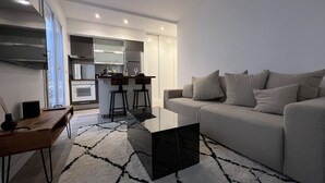 A modern living room with a sofa, a coffee table, and a kitchen area in the background. - Suite Luxueuse Avec Jardin Privatif et Jacuzzi (Paris)