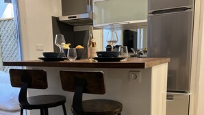 A modern kitchen with a built-in island, two bar stools, and a large refrigerator. - Suite Luxueuse Avec Jardin Privatif et Jacuzzi (Paris)