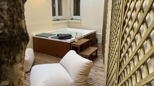 A cozy outdoor seating area with a wooden deck, a cushioned chair, and a hot tub. - Suite Luxueuse Avec Jardin Privatif et Jacuzzi (Paris)