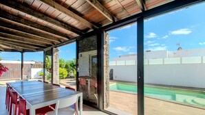 Un porche cubierto con piscina, una mesa y sillas, y un muro de piedra.