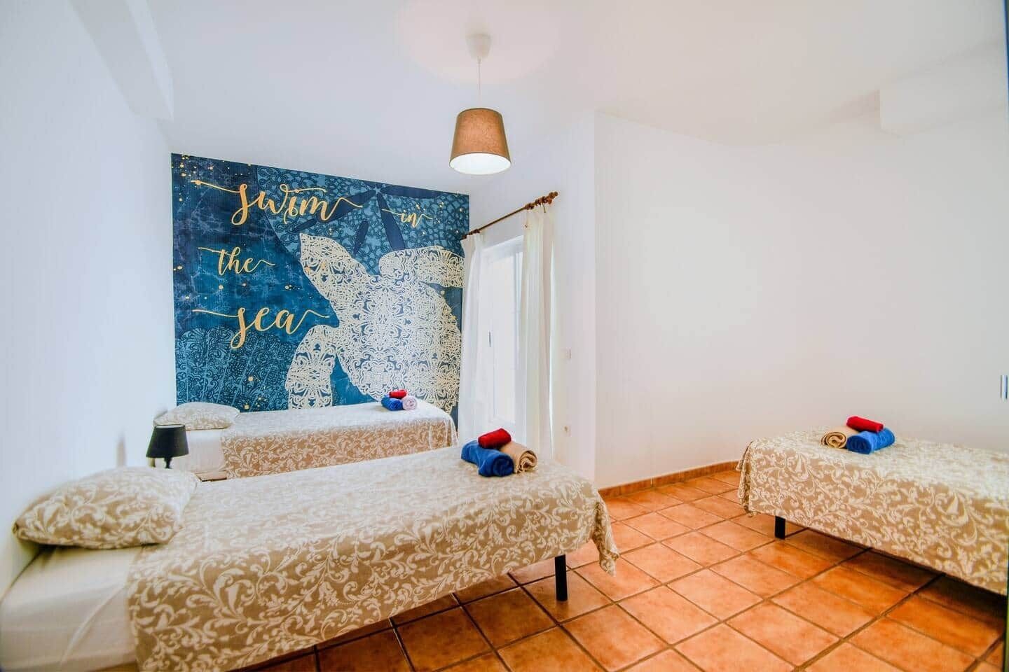 A room with two beds, a large wall mural, and a ceiling light.