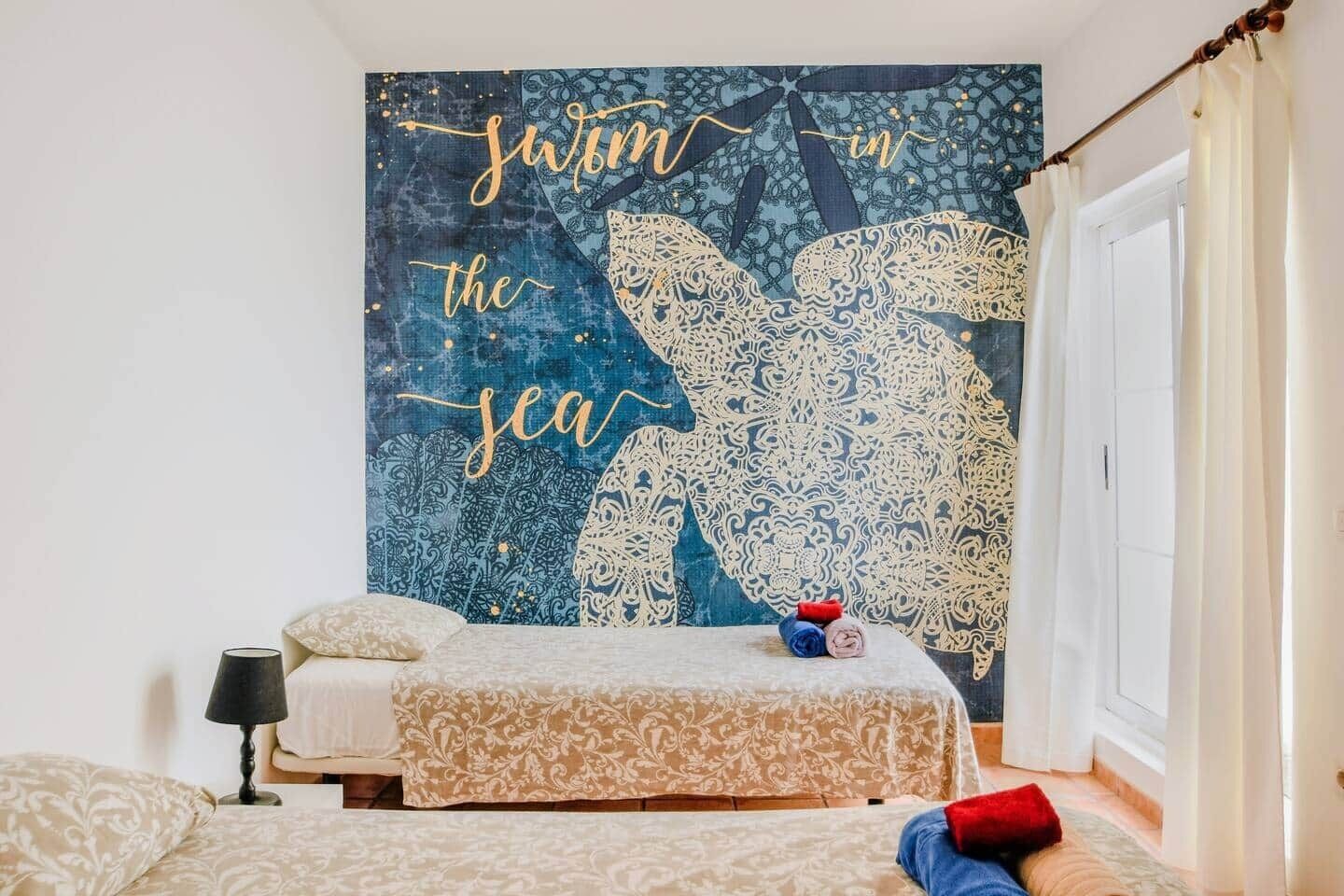 A bedroom with a bed, a bedside table, a lamp, and a wall tapestry.