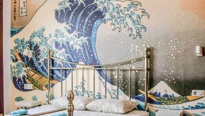Una cama con estructura metálica, una pared decorada con un cuadro de olas y una pequeña estructura similar a un santuario.