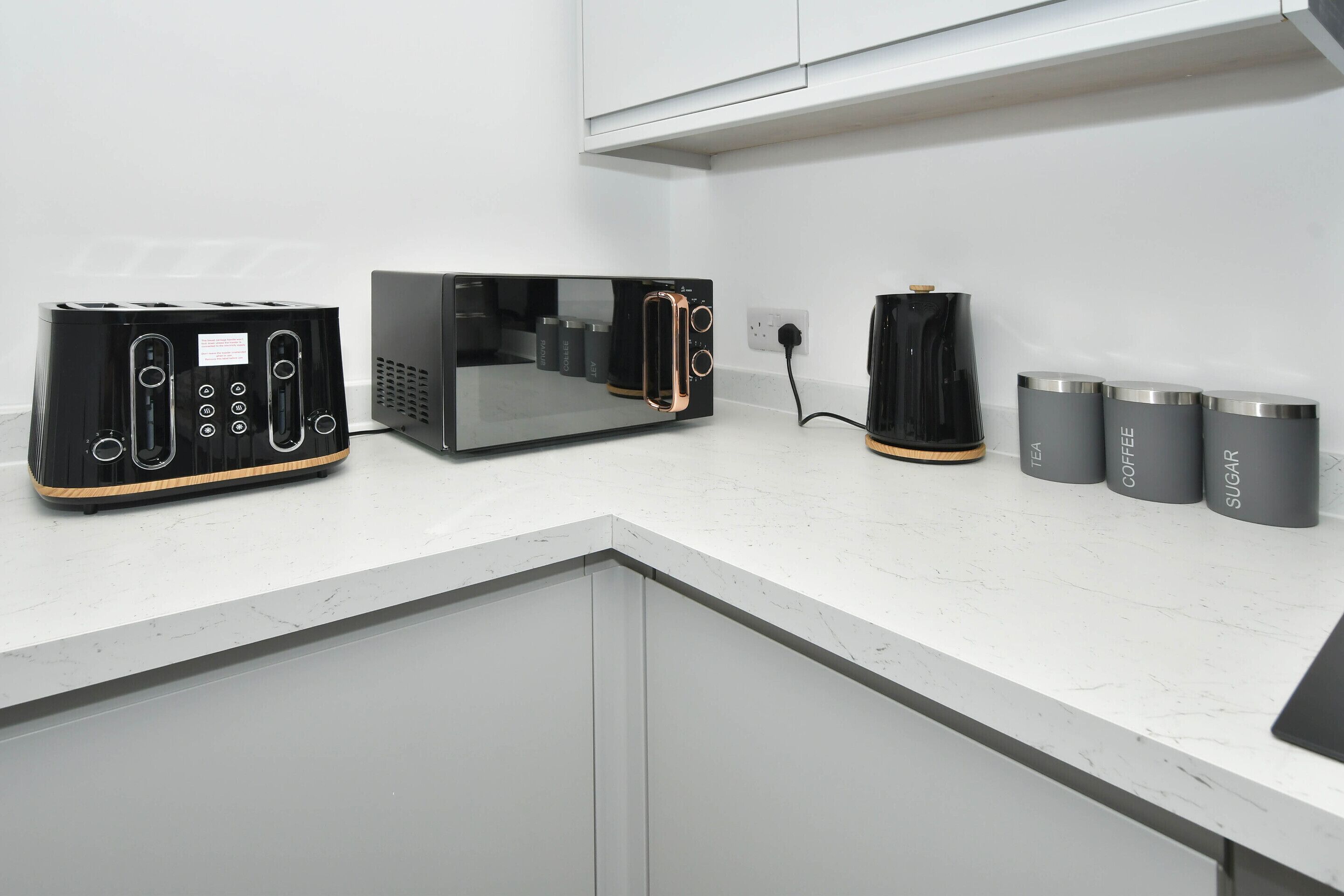 Una cucina con un tostapane, una macchina per il caffè e tre contenitori etichettati con tè, caffè e zucchero.
