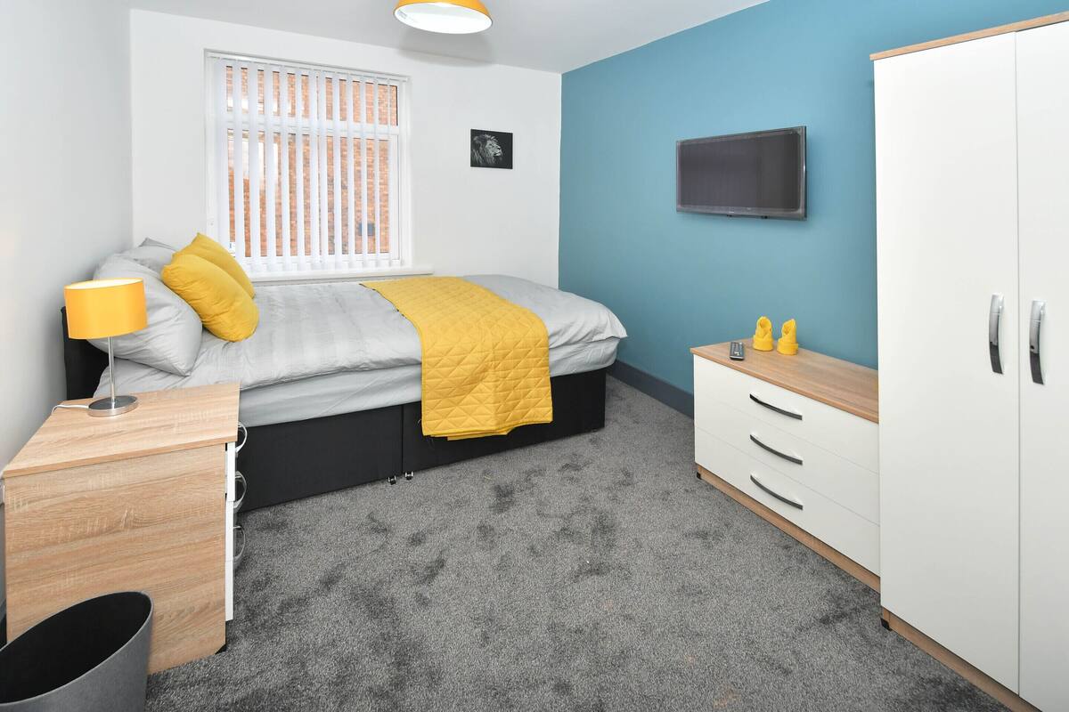 Une chambre à coucher comprenant un lit, une table de chevet, une armoire et une fenêtre avec des stores.