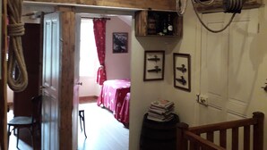 Quarto rústico com vigas de madeira aparentes, um mezanino para dormir e uma pequena mesa com uma cadeira.