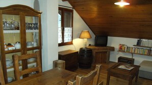 Um quarto aconchegante e rústico com mobiliário de madeira, uma mesa de jantar, cadeiras, uma estante e uma televisão.