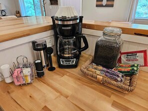 Eine Küchenarbeitsplatte mit einer Kaffeemaschine, einem Einmachglas schwarzer Bohnen, einer Snackkorb und einer Tüte Mikrowellen-Popcorn.