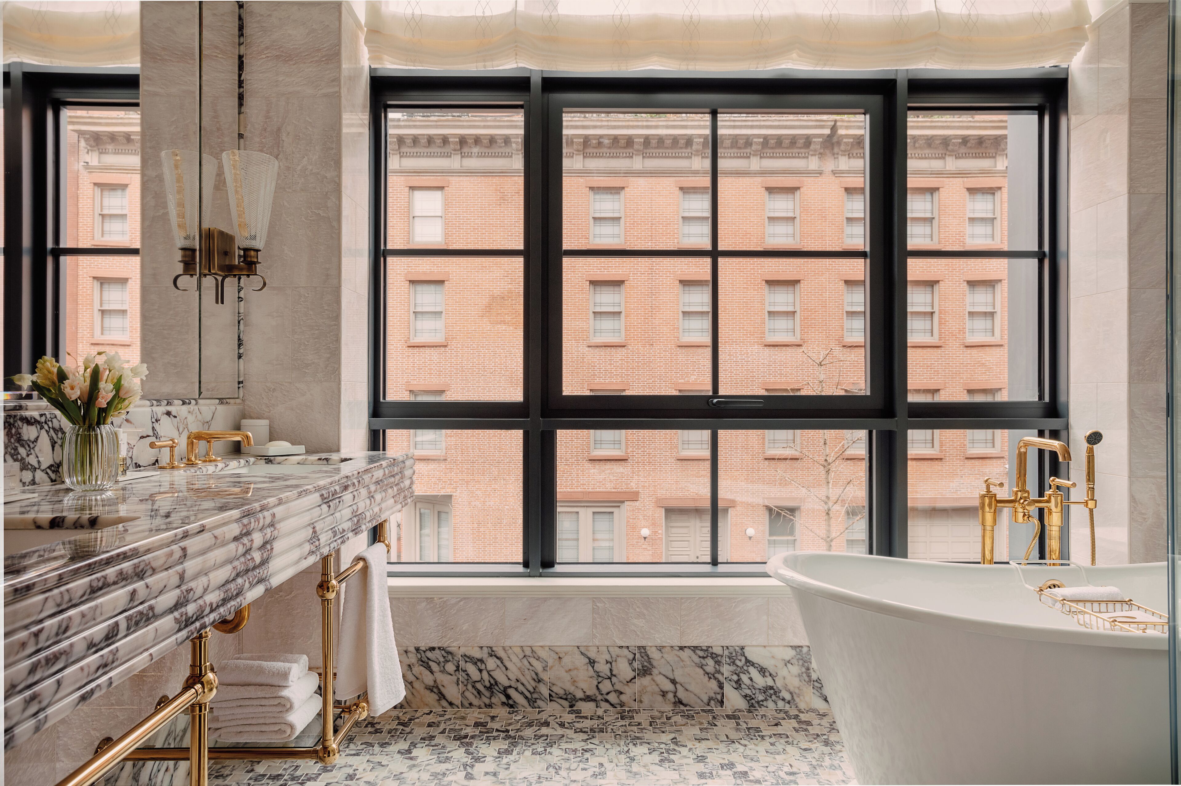 Un bagno con un'ampia finestra, un lavandino in marmo, una vasca da bagno indipendente e un porta asciugamani.