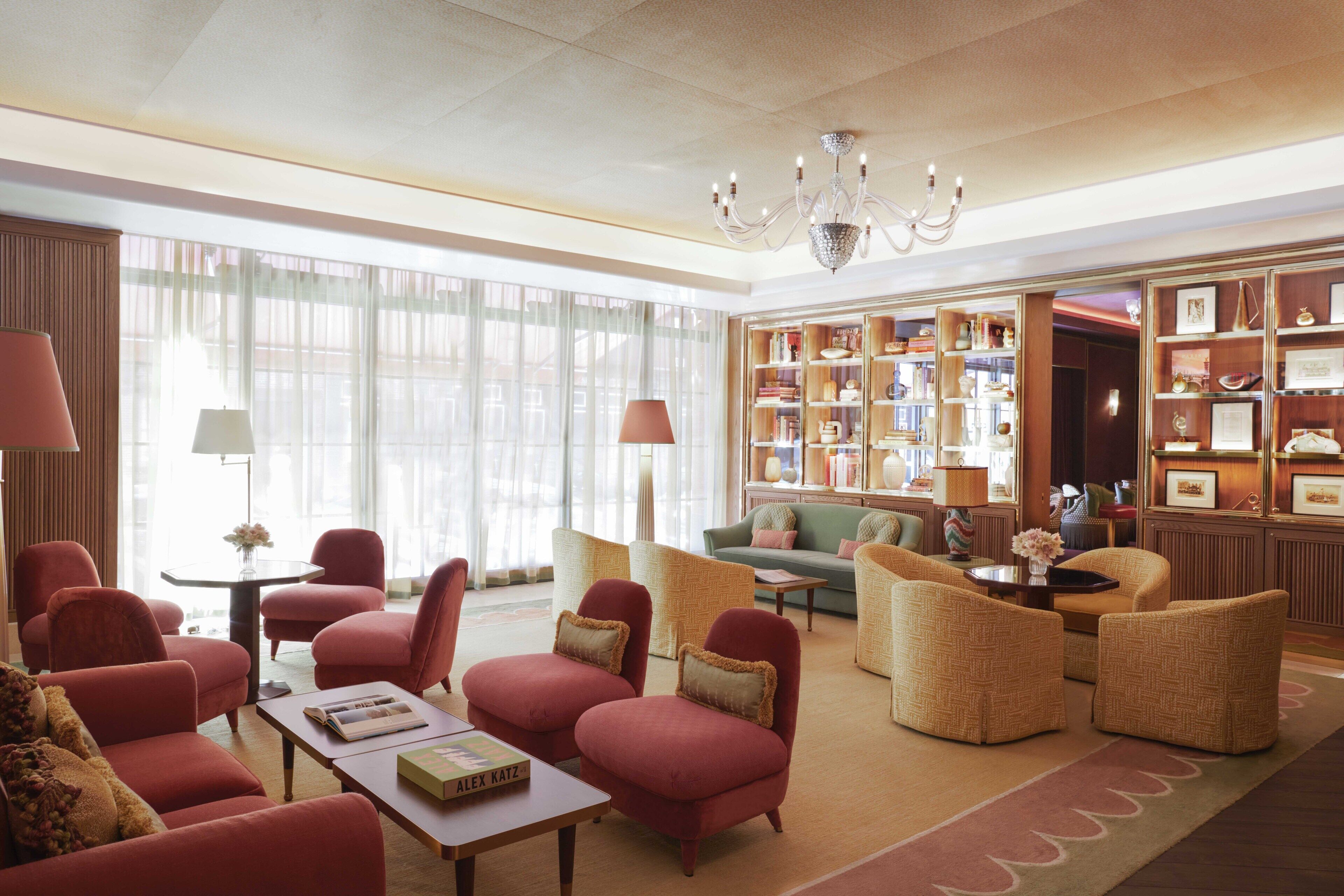 A spacious lobby with a variety of seating options, including red armchairs and wicker sofas, a central coffee table, and a chandelier.
